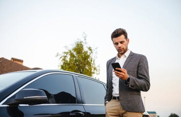 Man staat naast zijn auto en kijkt op zijn telefoon