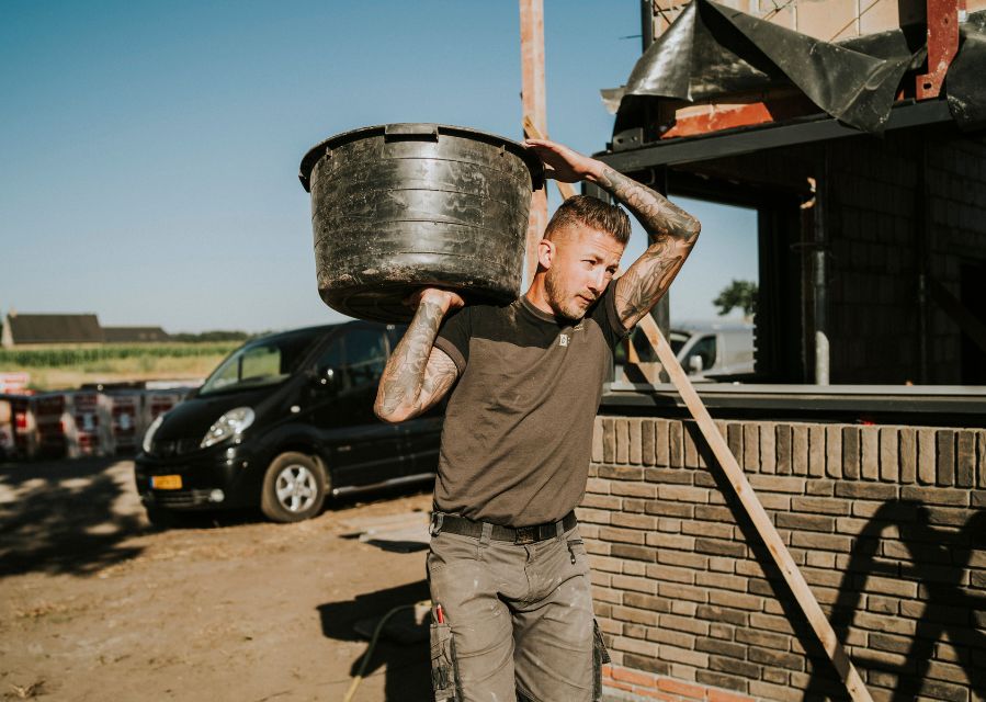 Een man draagt een speciekuip op zijn schouder in de bouw