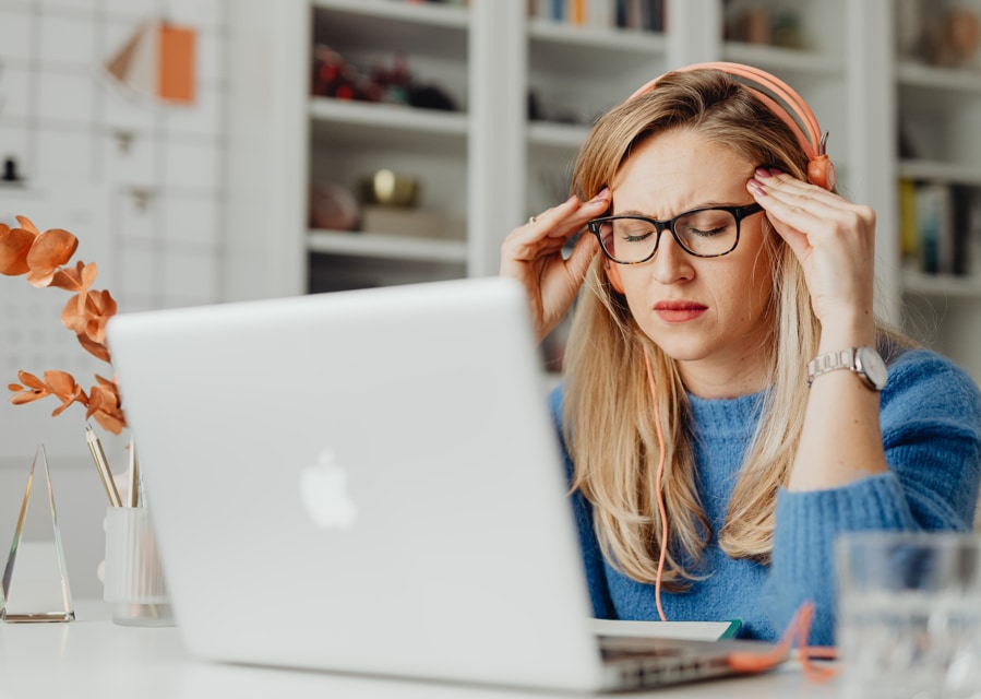 Vrouw die achter de laptop zit en zichtbaar hoofdpijn heeft