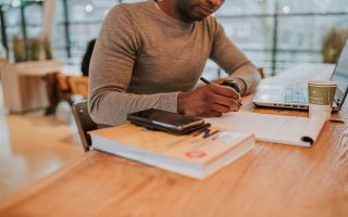 Man werkt achter laptop en schrijft op zijn schrijfblok.