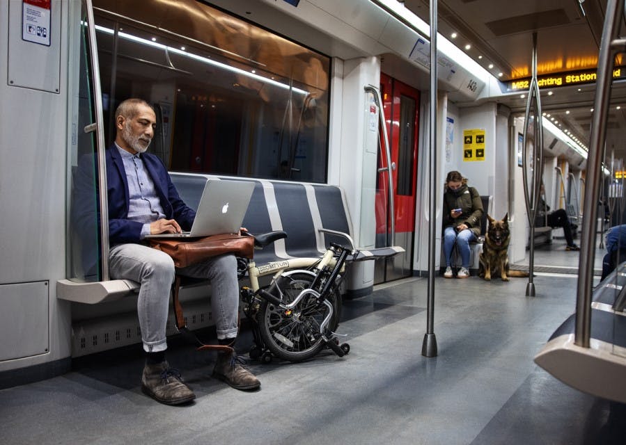 man die in de metro zit en op zijn laptop aan het werk is
