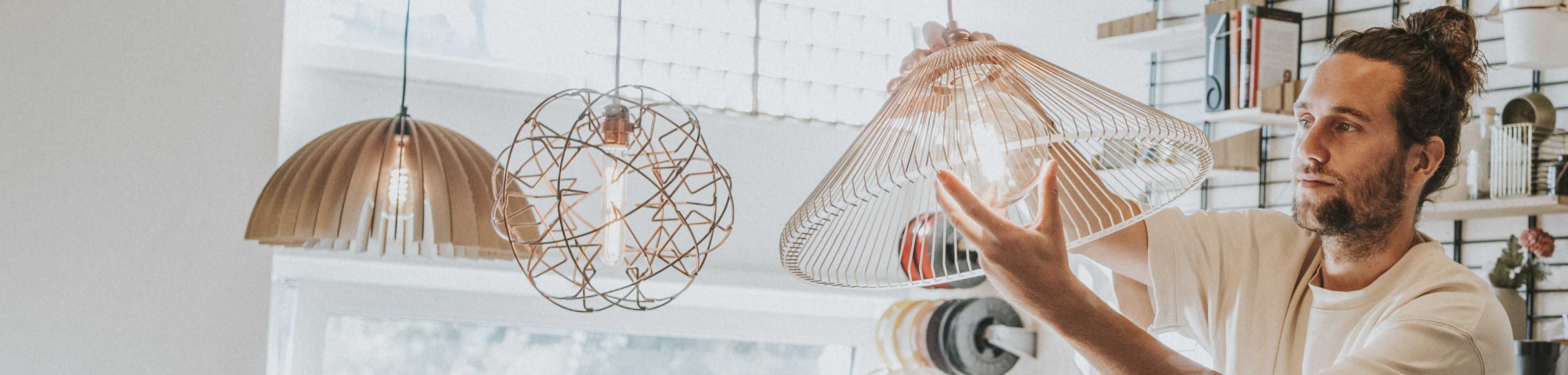 Een man draait in een lampenwinkel een filamentlamp in een hangend armatuur.