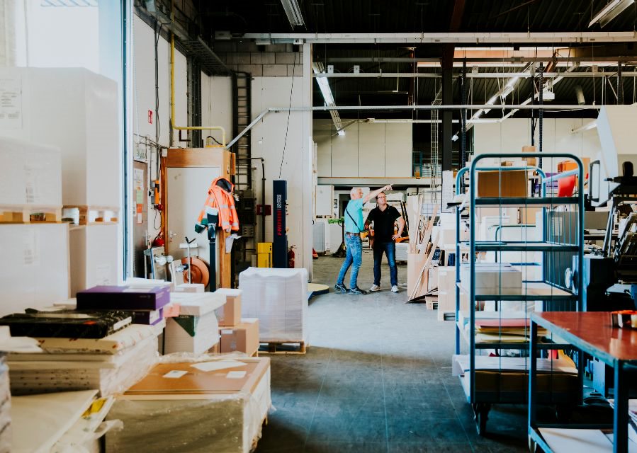 Twee mensen staan in een bedrijfsruimte tussen stellingen en bedrijfsmaterialen.