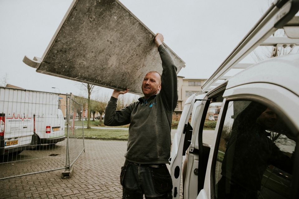 Een man tilt een steigerplank uit zijn bestelauto