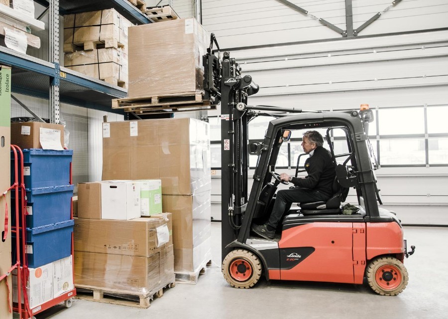 Een man zet met een heftruck een pallet met dozen op een andere pallet met dozen.