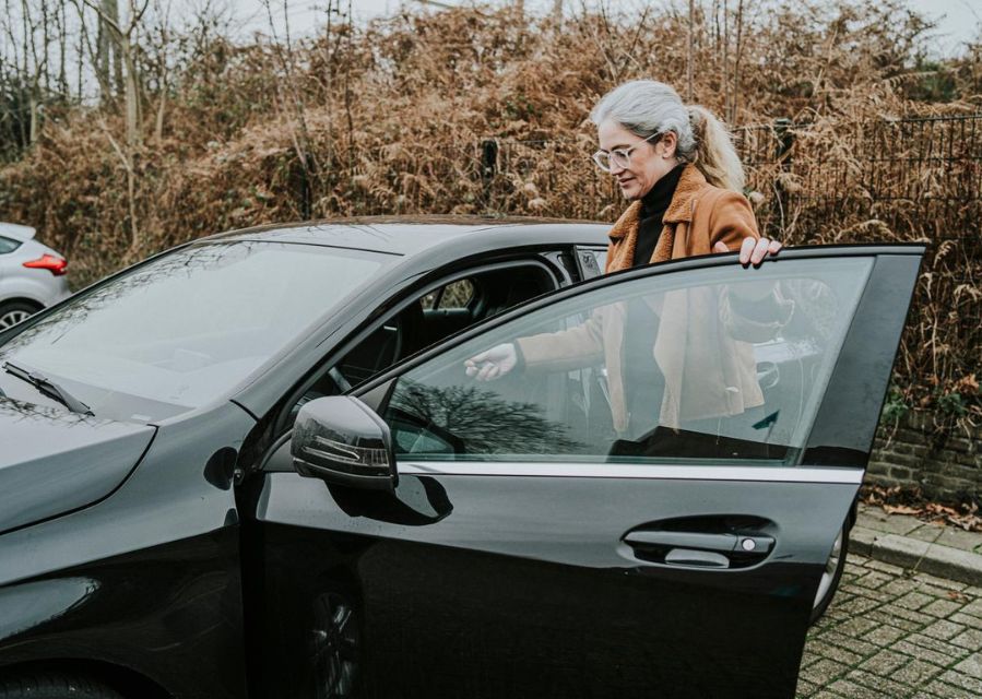 Een vrouw stapt via het geopende portier in aan de bestuurderskant van een zwarte personenauto. 