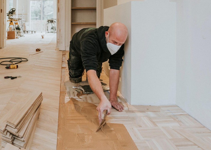 Een man legt een vloer verlijmd, met een stofmasker op