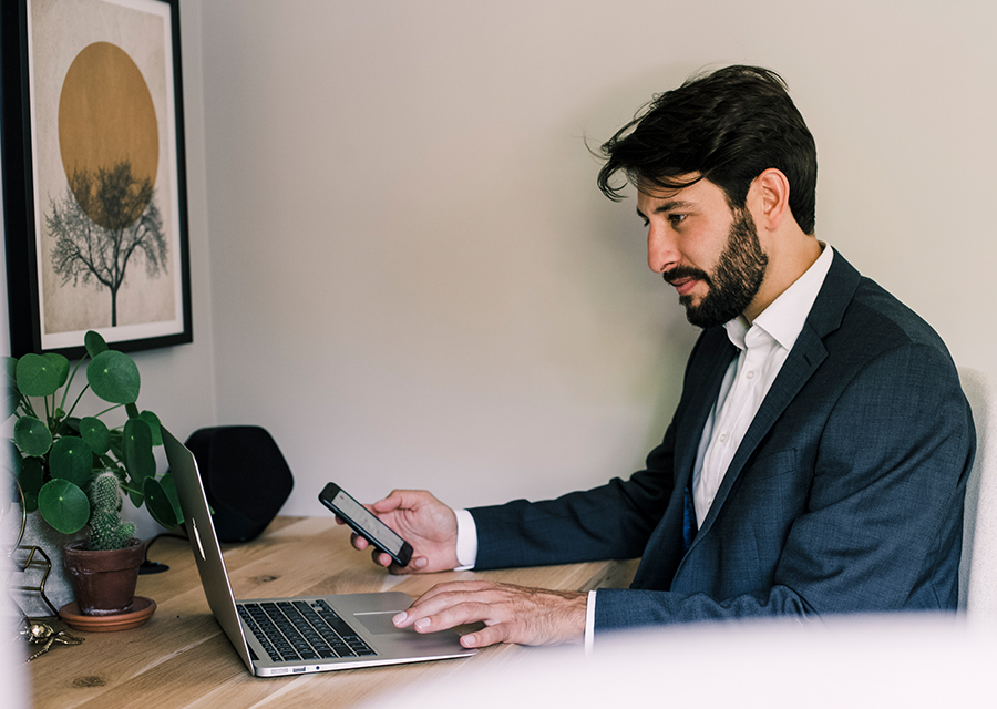 Man werkt achter laptop en heeft telefoon vast