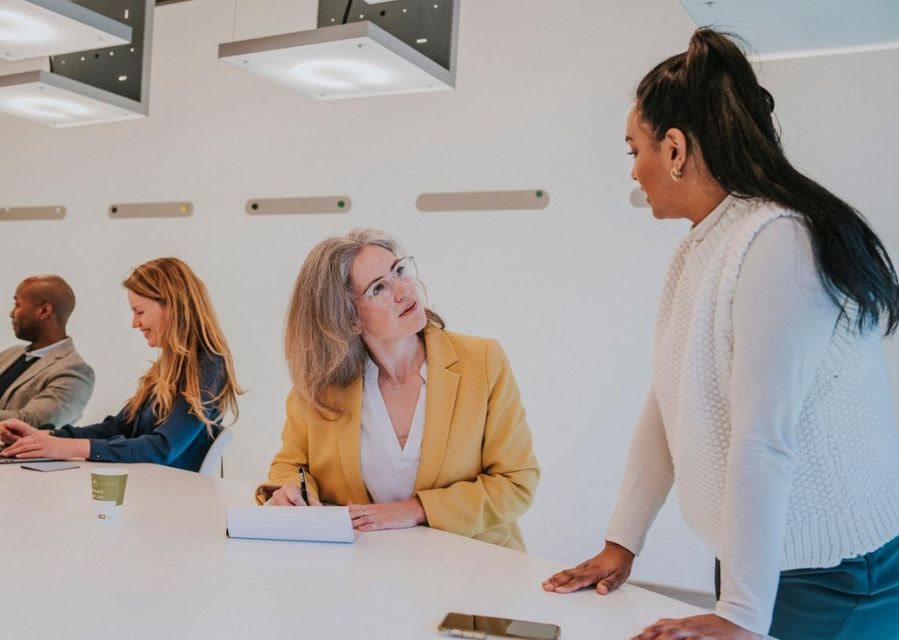 4 mensen zitten naast elkaar tijdens een bespreking in een overwegend witte kantoorruimte.