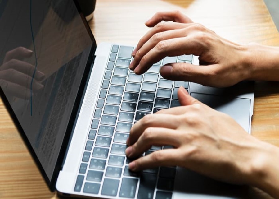 Twee handen typend op een laptop die op tafel staat