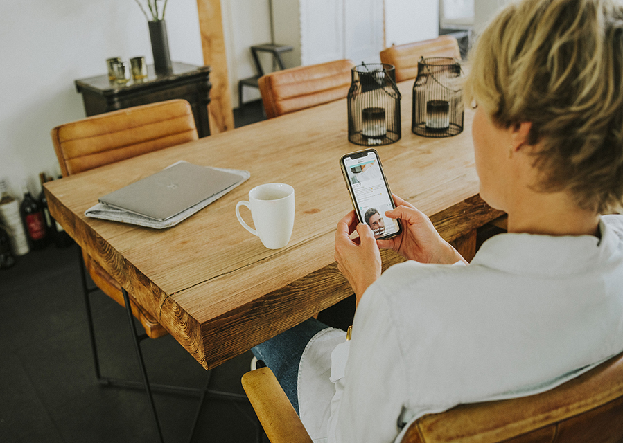 Een vrouw zit met haar telefoon in de hand aan tafel.