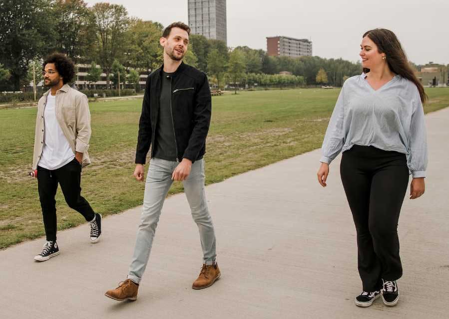 Een vrouw en 2 mannen lopen lachend door een park