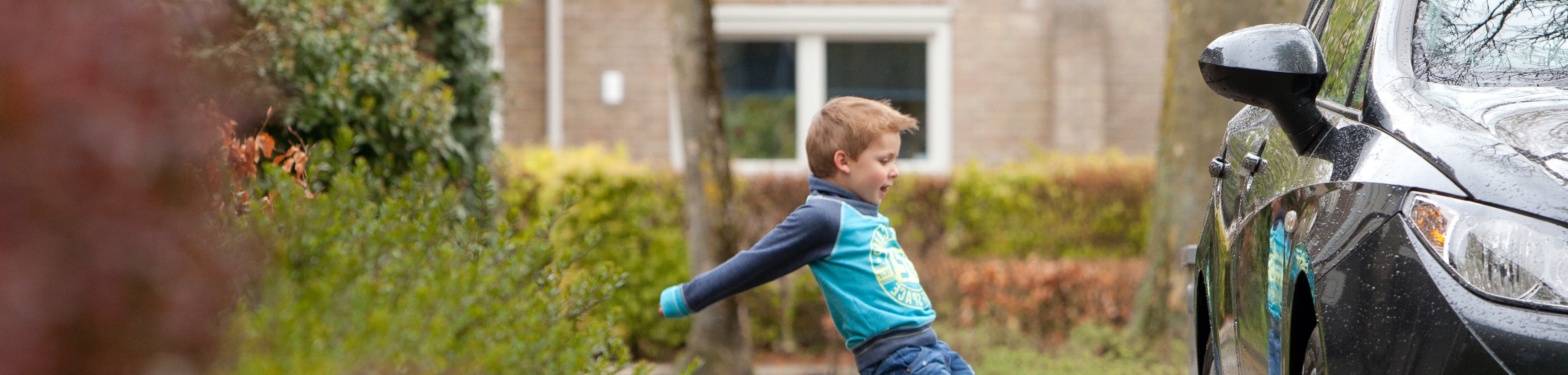Jongetje die een bal tegen een auto aanschiet tijdens het spelen