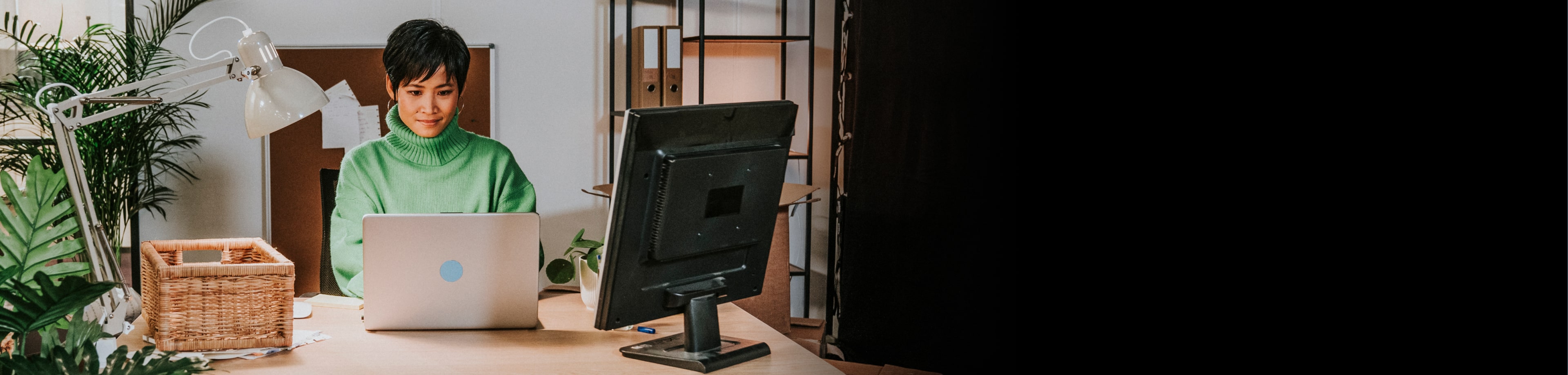 Vrouw die aan een bureau zit en op haar laptop werkt.