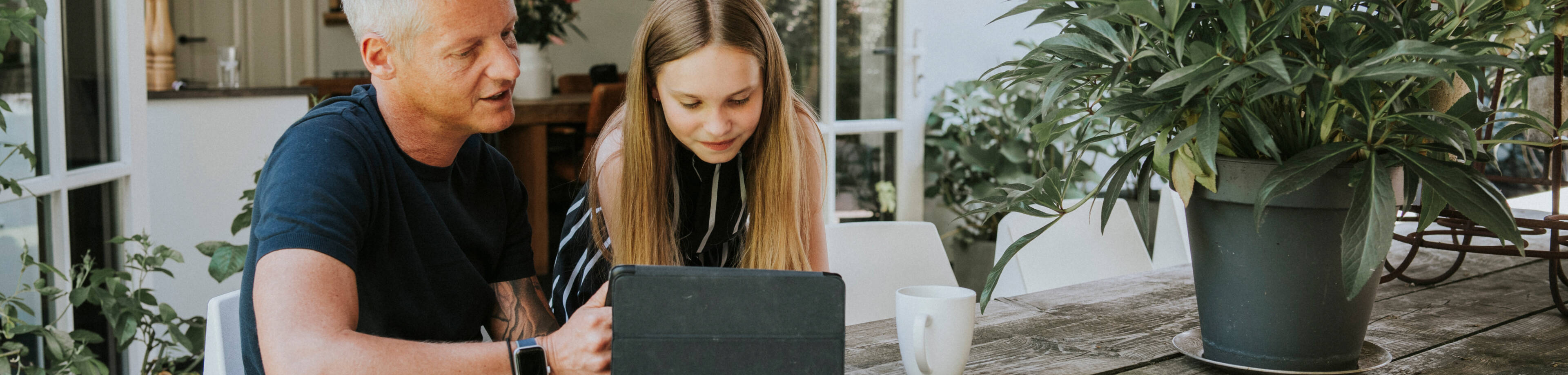 Een vader en zijn dochter zitten aan tafel op de tablet te kijken.