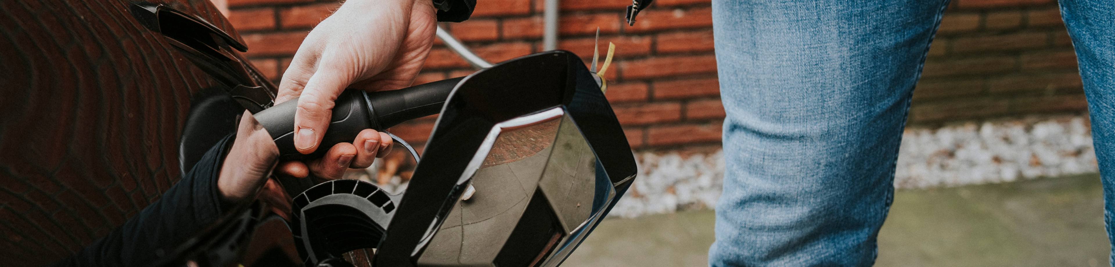 Iemand die zijn elektrische auto aan de laadkabel legt. De elektrische auto is verzekerd met een Interpolis autoverzekering.