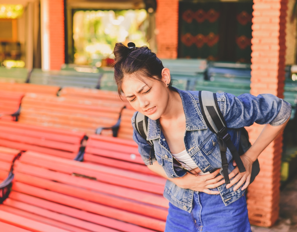 Aziatisch meisje heeft buikpijn in het buitenland. Met de aanvullende dekking geneeskundige kosten van Interpolis verzekert u uw medische kosten tijdens uw reis in het buitenland die uw zorgverzekering niet vergoedt. 