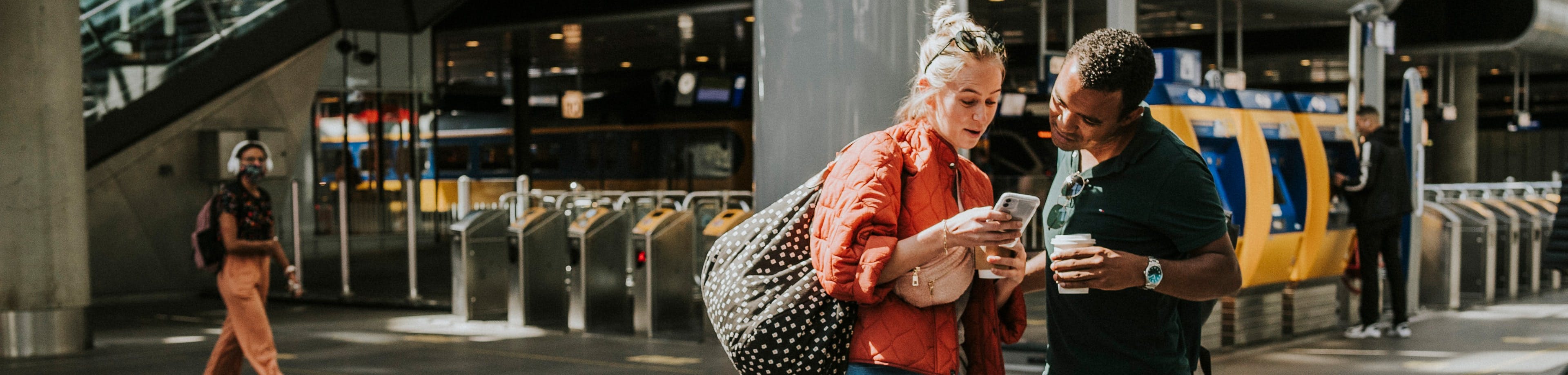 Man en vrouw die op reis gaan en op het station op hun smartphone een reisverzekering kiezen