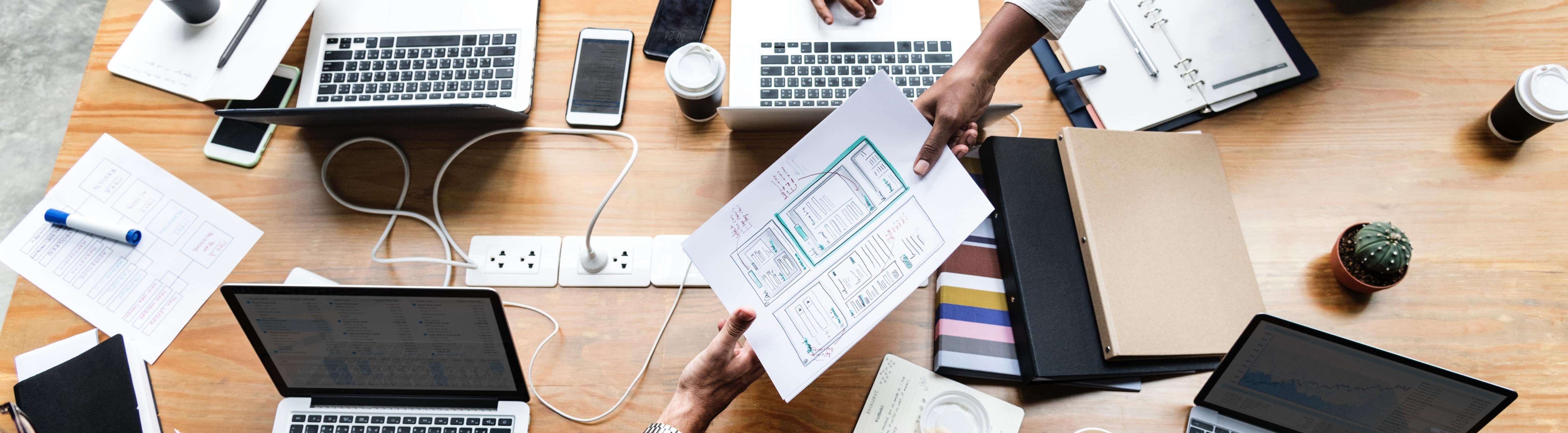 Vergadertafel met laptops, koffie en schrijfblokken erop. Met ZekerInBedrijf van Interpolis verzekert u uw bedrijf tegen onverwachte gebeurtenissen.