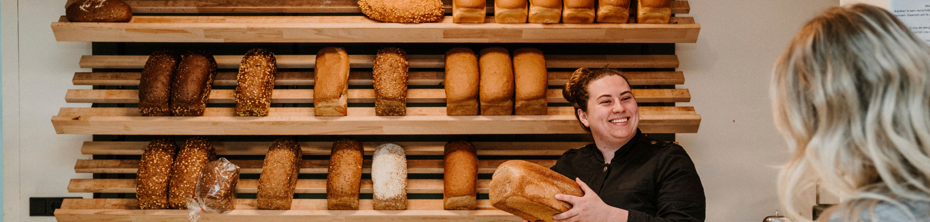 Vrouw koopt een brood van een lachende bakker