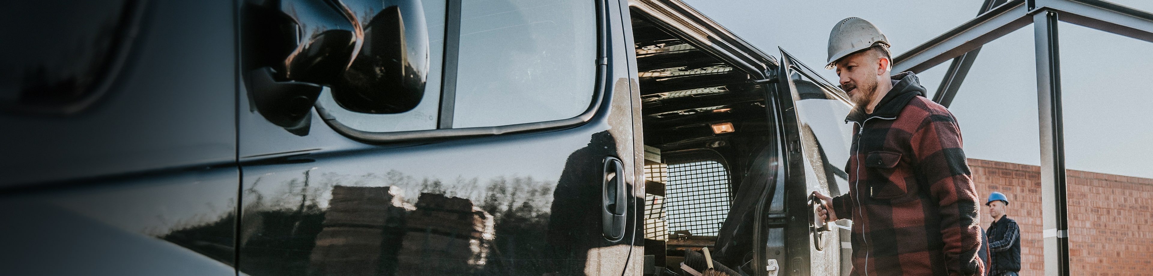 Man met bouwhelm loopt op een bouwplaats naar een busje en opent de deur