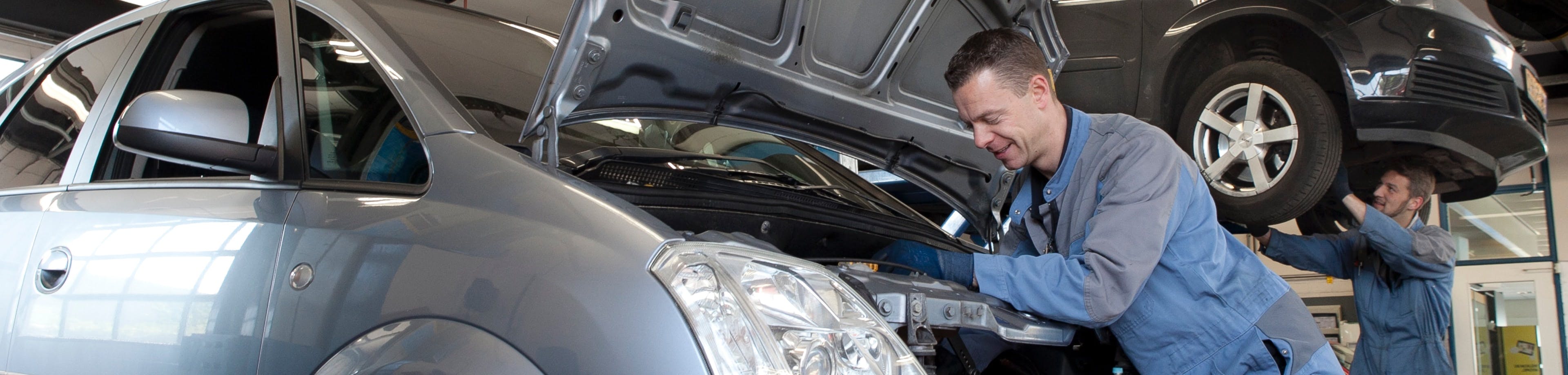 Een werknemer van een garage sleutelt aan een auto. Met de Klantvoertuigenverzekering verzekert u schade aan of door voertuigen van klanten die u repareert of bewerkt.