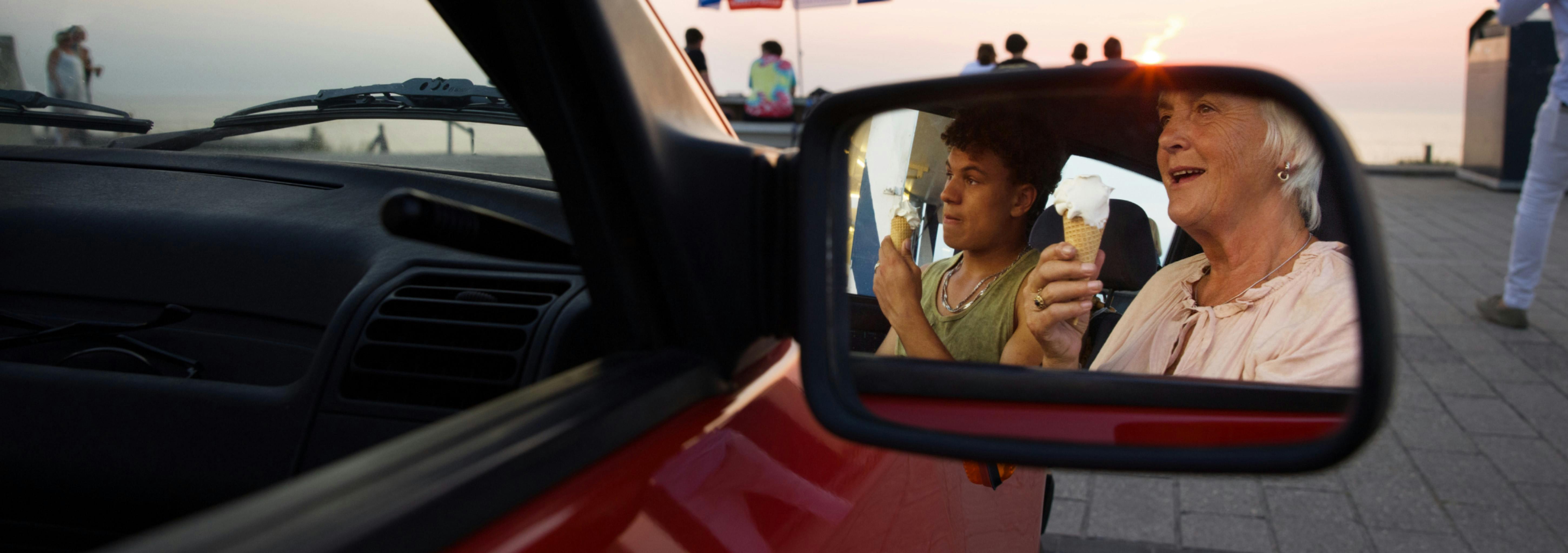 Vrouw en haar kleinzoon in een stilstaande auto, gezien via de zijspiegel