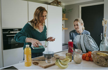 Een vrouw staat in de keuken en schenkt yoghurt in een kom als voorbereiding voor het ontbijt.