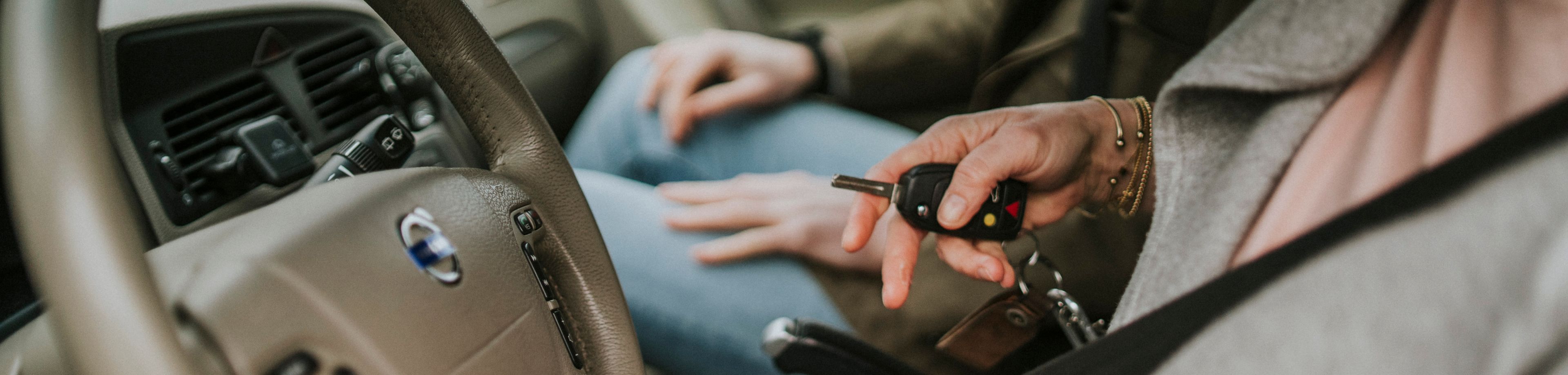 Vrouw zit achter het stuur van een auto, met de autosleutel in haar hand