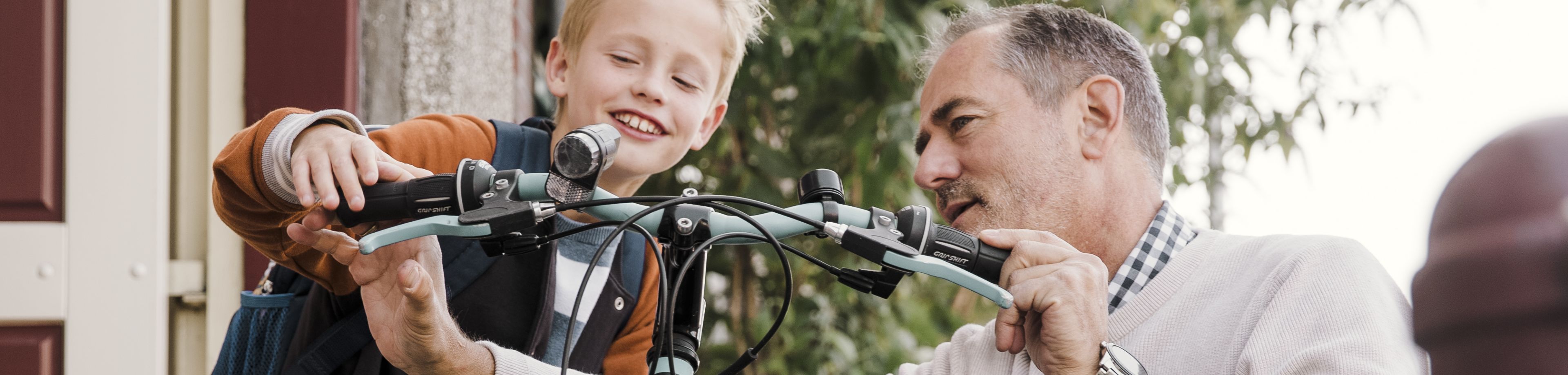 Een man en kind houden samen een kinderfiets vast.