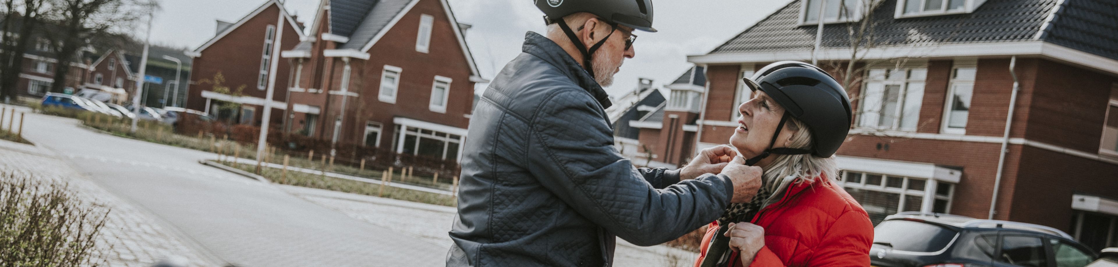 Man en vrouw staan naast e-bikes en zetten fietshelmen op.
