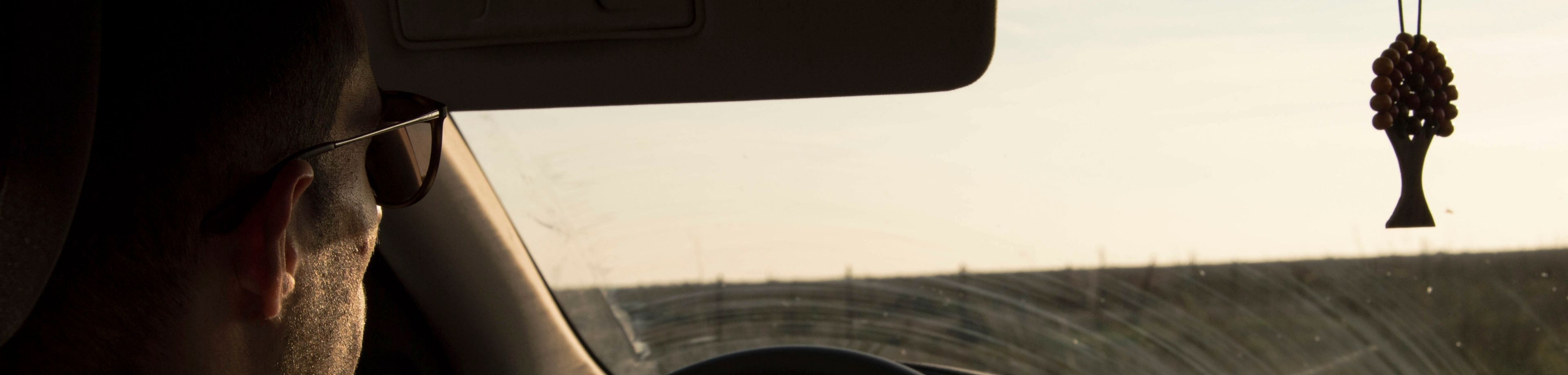 man die aan het autorijden is terwijl de zon die op de voorruit schijnt