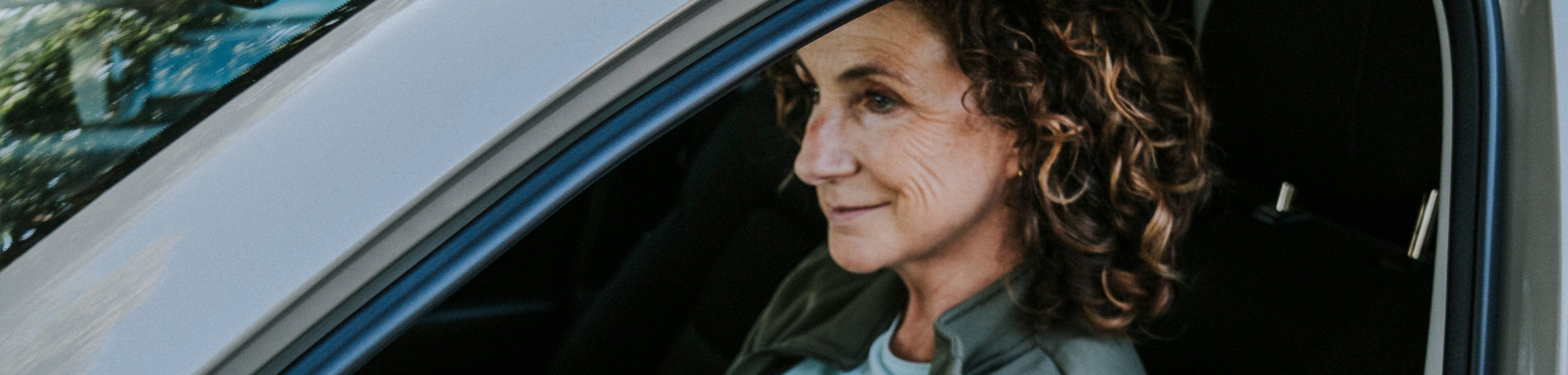 Een vrouw zit achter het stuur van een stilstaande auto, met het portier open