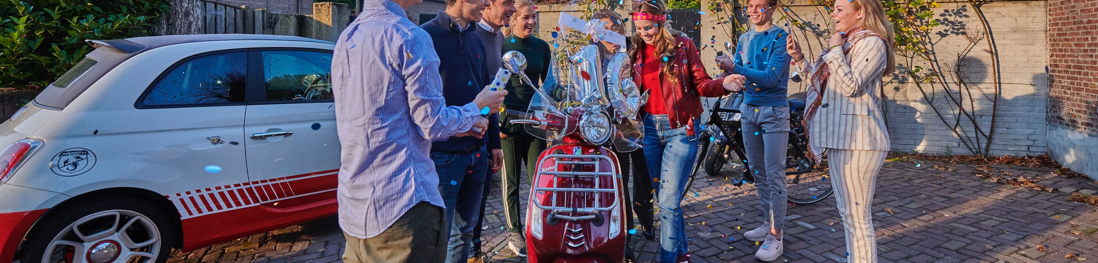 Een groep mensen om een scooter die iemand krijgt voor zijn verjaardag