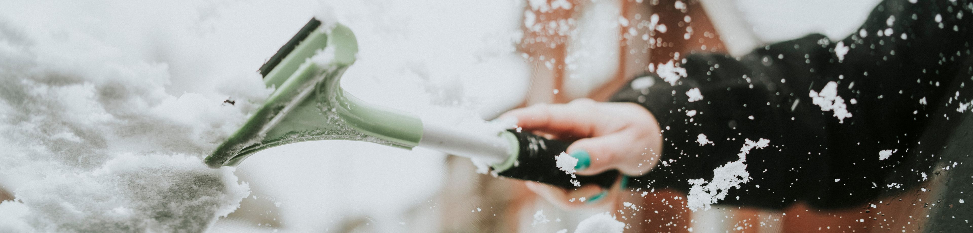 Iemand haalt met een krabber sneeuw van de vooruit