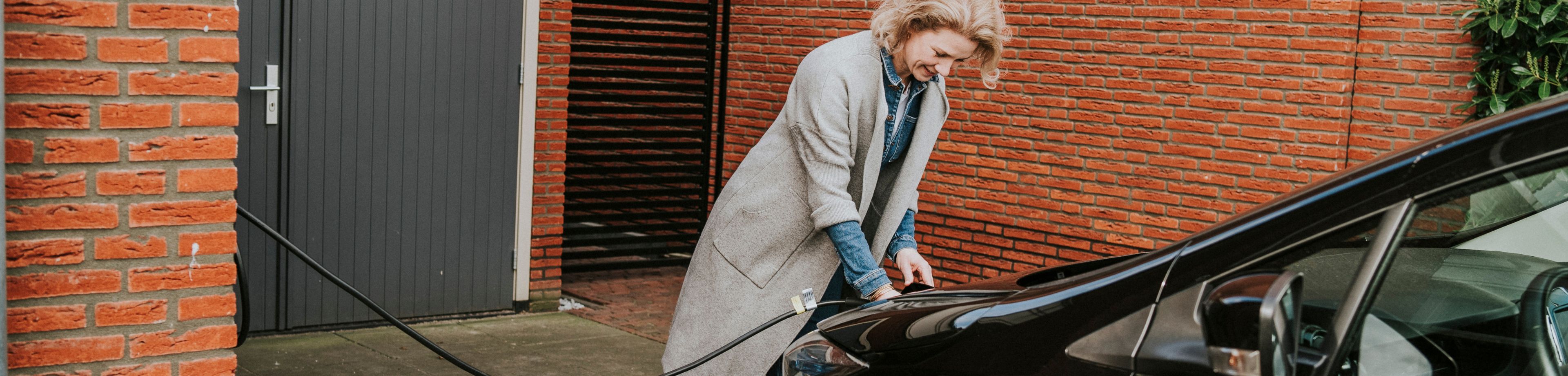 Een vrouw steekt de stekker van de laadkabel in de voorkant van haar elektrische auto.