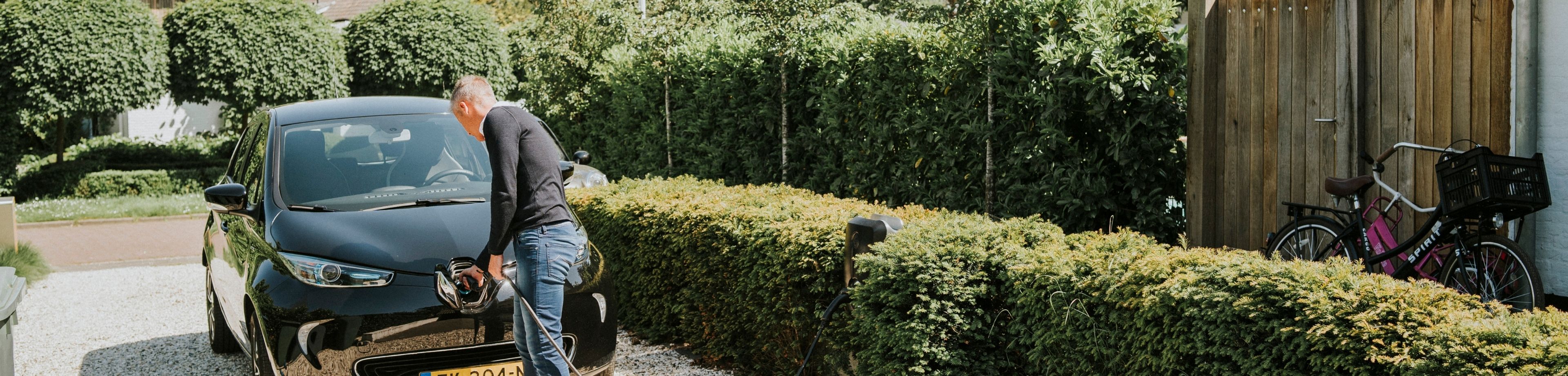 Een man steekt de stekker in de voorkant van zijn elektrische auto.