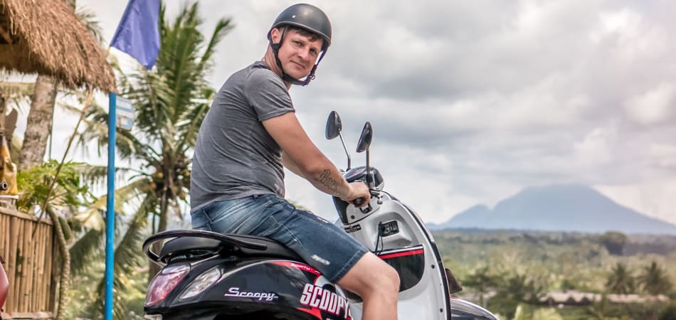 Een man in het buitenland die op een huurscooter zit en een helm draagt