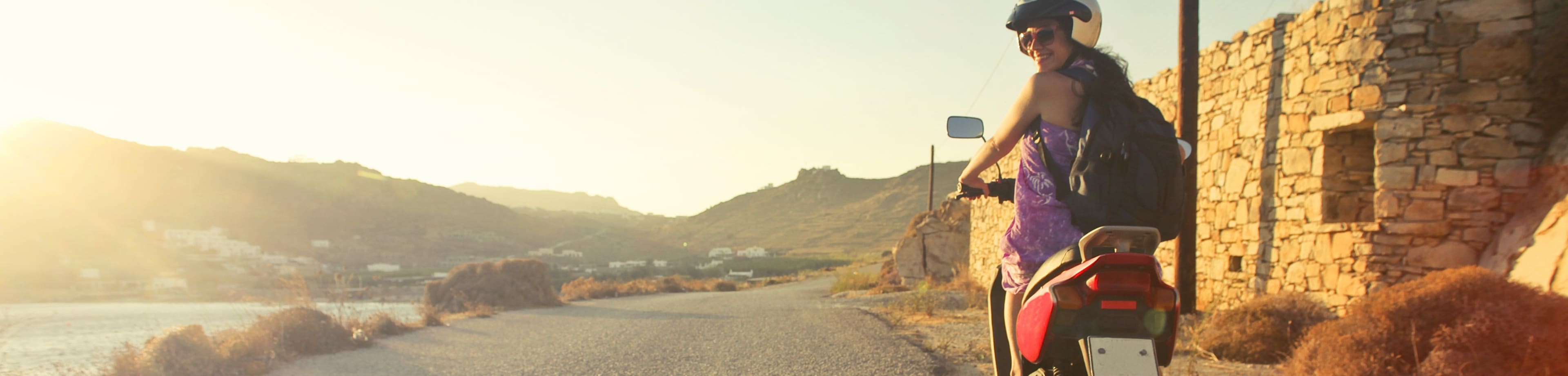 Een toerist die wegrijdt op een scooter en achterom kijkt