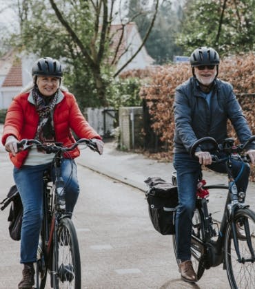 Een man en vrouw met fietshelm op fietsen op elektrische fietsen.