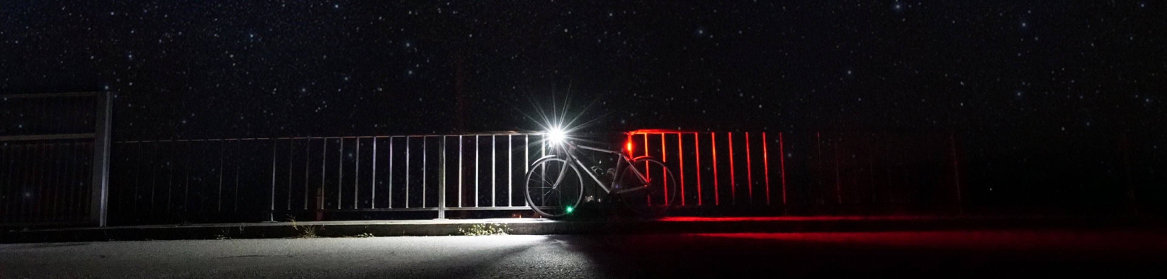 Een fiets met brandend voorlicht en achterlicht die tegen een hek aanstaat