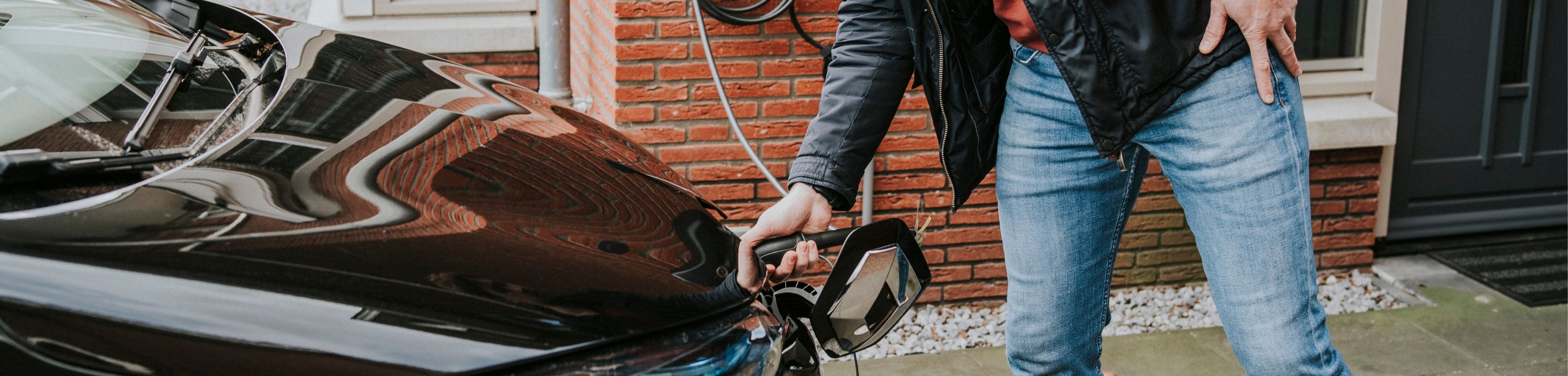 Persoon laadt zijn elektrische auto op. Verzeker je een elektrische auto anders dan een brandstofauto?