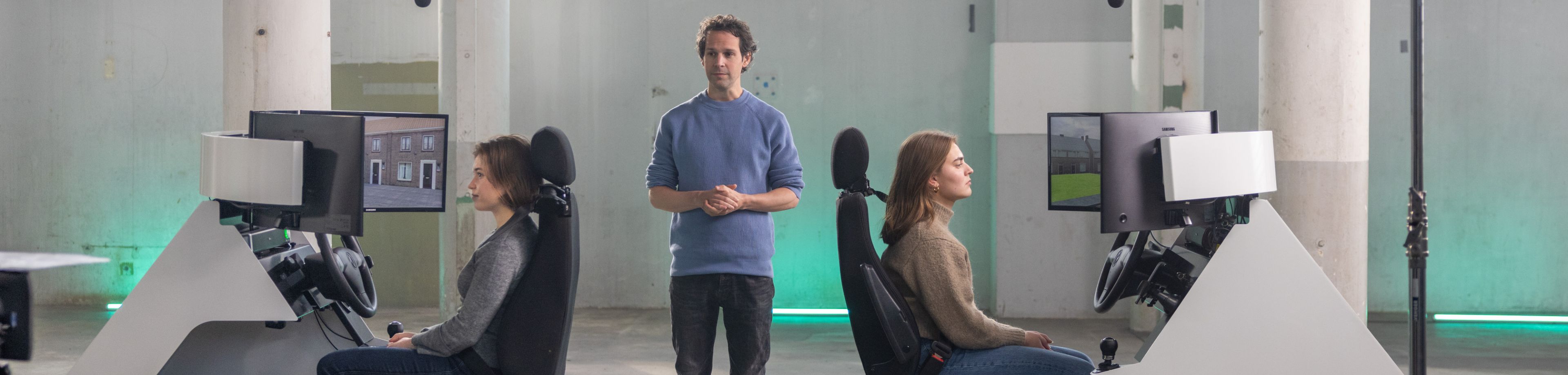 Victor Mids staat tussen 2 deelnemers van de BewustBestuurd video in en geeft aanwijzigingen.