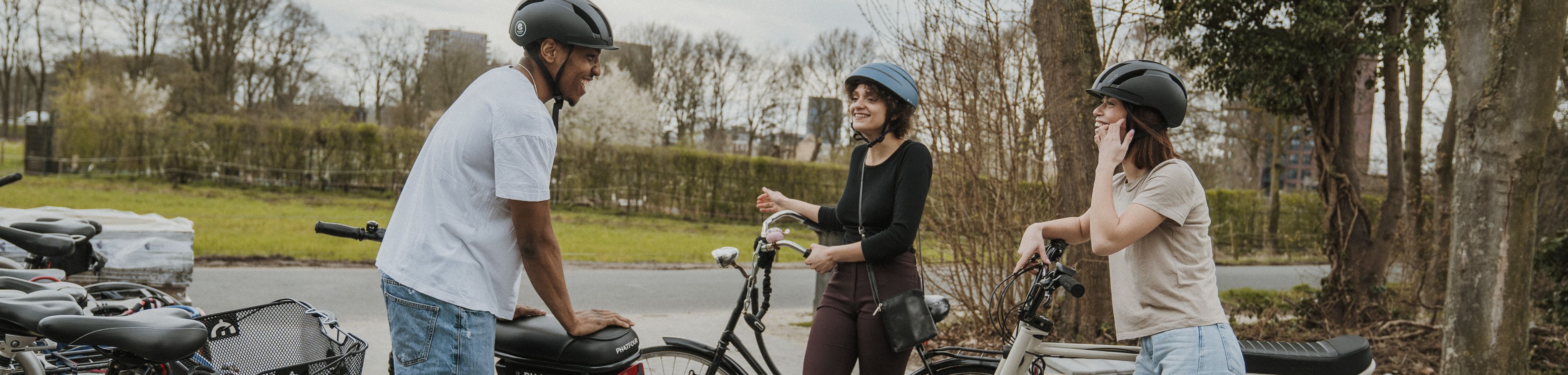 3 jongeren met fietshelm op staan naast hun fietsen en brommer en zijn in gesprek met elkaar.