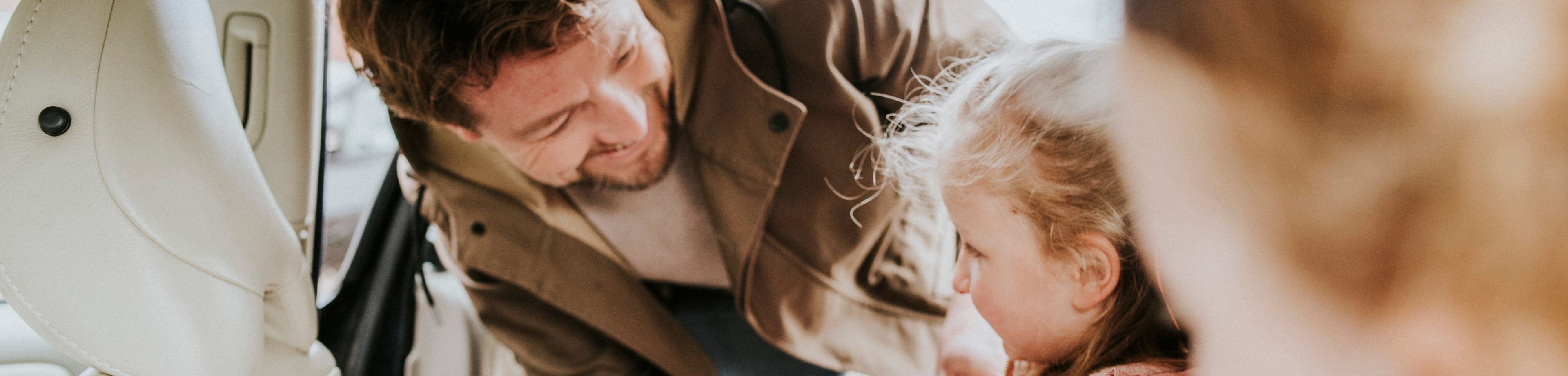 Een vader doet de veiligheidsgordel om bij zijn dochter, die in de auto zit. 