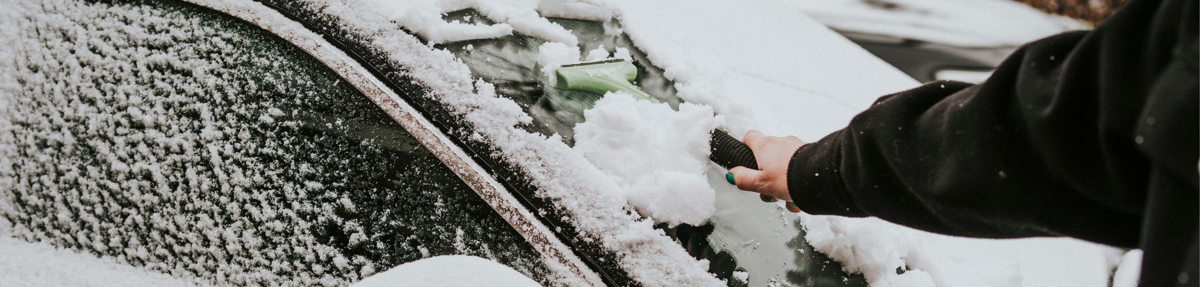 Iemand haalt met een ijskrabber sneeuw van de vooruit van een auto