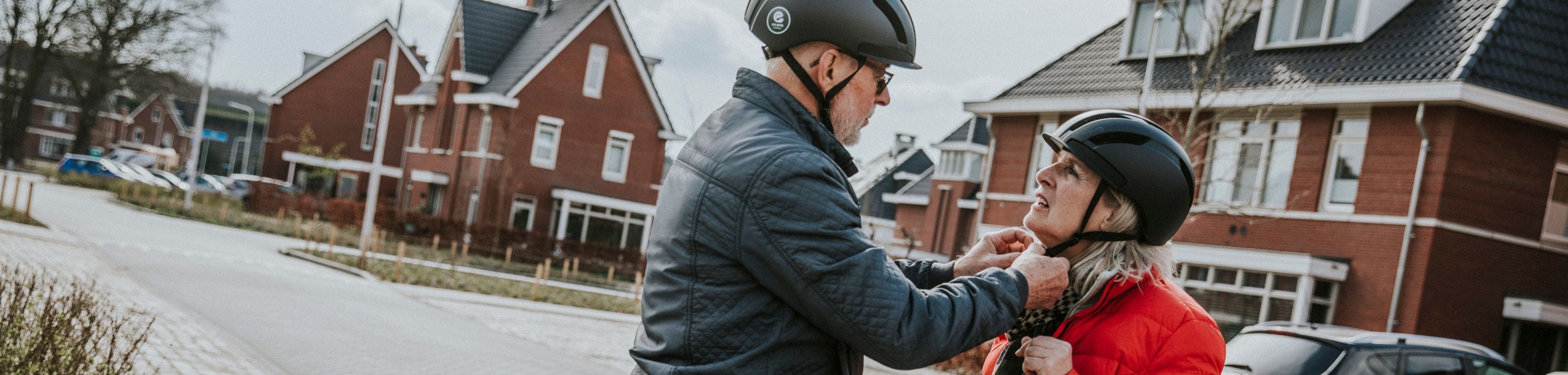 Man doet bij vrouw het gespje van de fietshelm vast. Wist jij met een helm veel veiliger fietst op een e-bike? 