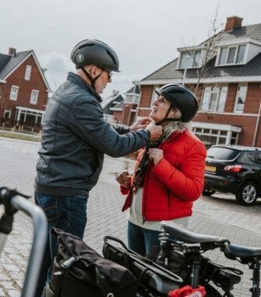 Man doet bij vrouw het gespje van de fietshelm vast. Wist jij met een helm veel veiliger fietst op een e-bike? 