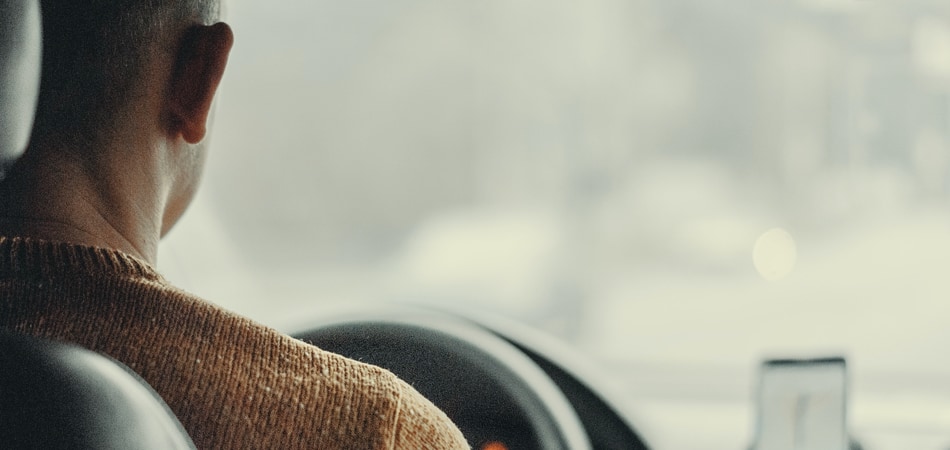 Man in een auto achter het stuur, met een smartphone in een houder