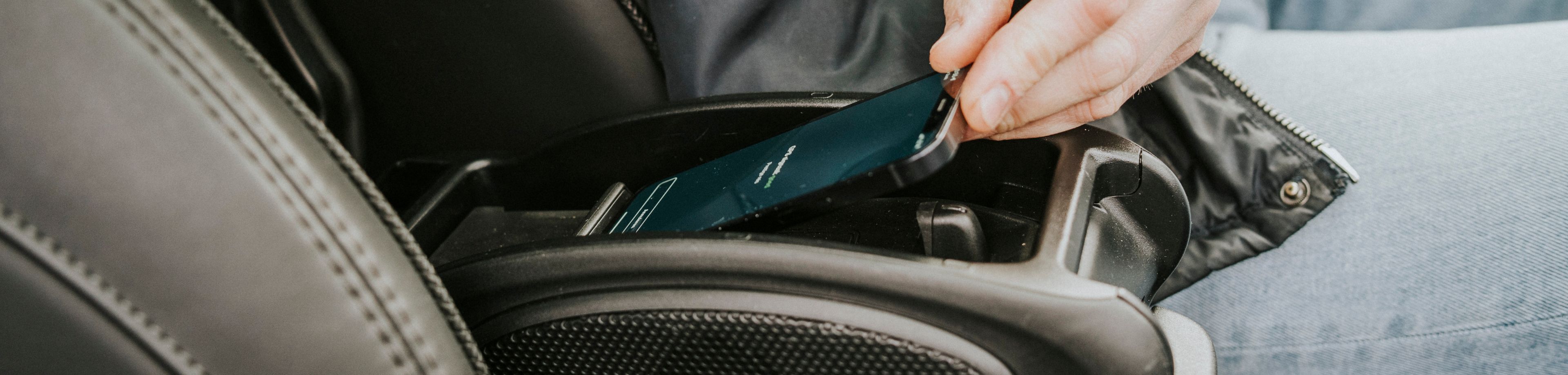 Iemand zit in de auto met de hand aan een telefoon die in de midden console ligt